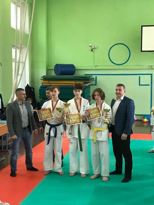 Young Dmitrii with teammates holding karate trophies and certificates in a gym